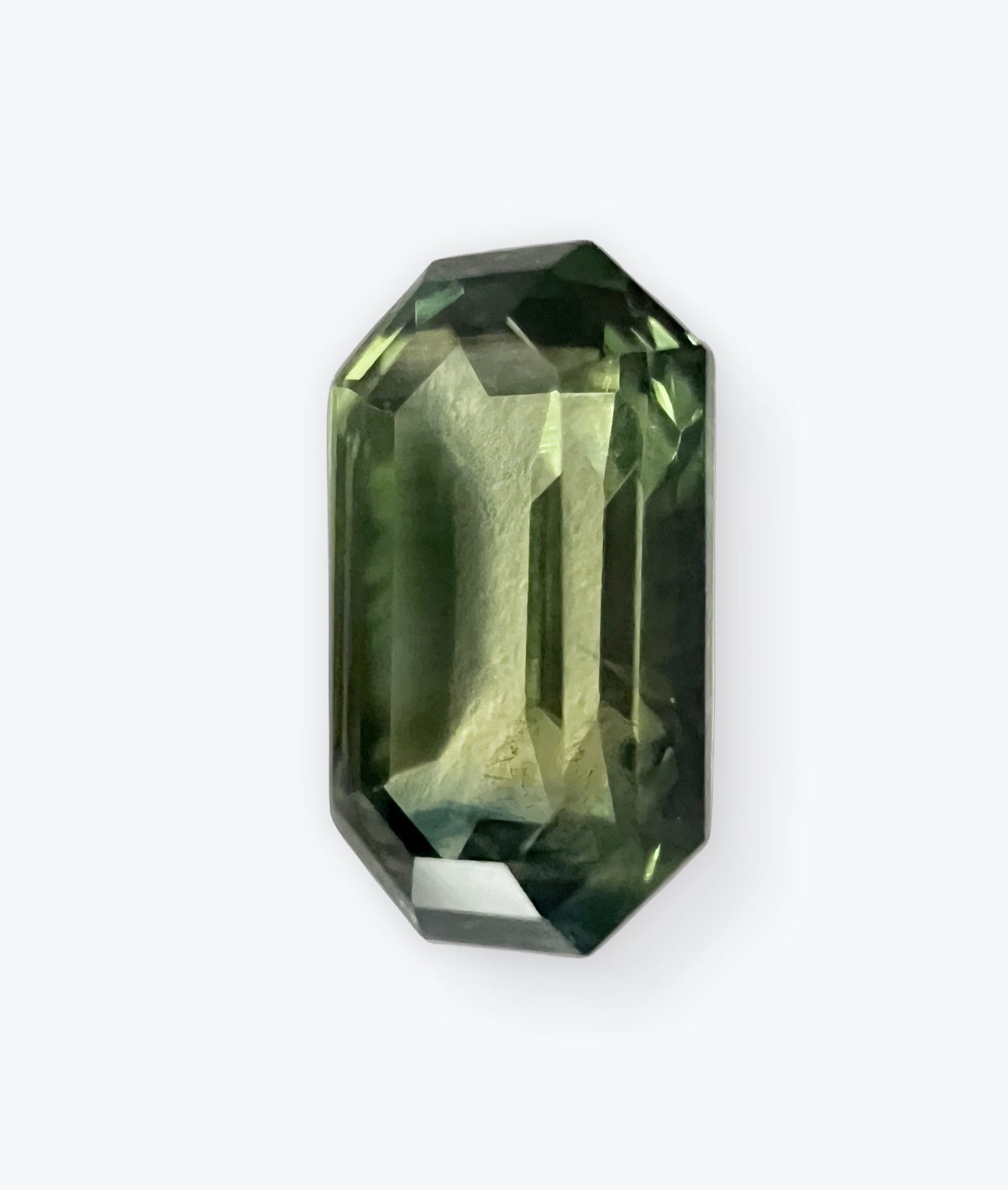 Close-up of a natural emerald cut teal blue sapphire gemstone, showcasing its deep greenish-blue hues and precision-cut facets.