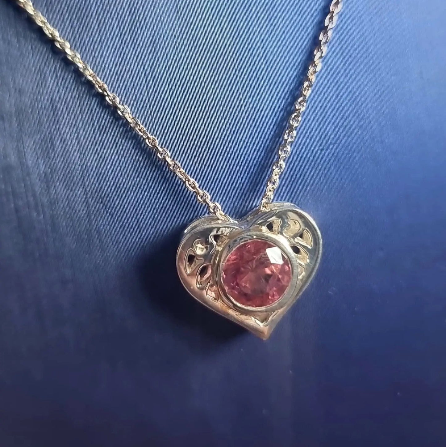 Tourmaline Gold Heart Pendant in 18K gold with a vivid pink gemstone, displayed on a dark background to emphasize its brilliance and craftsmanship.