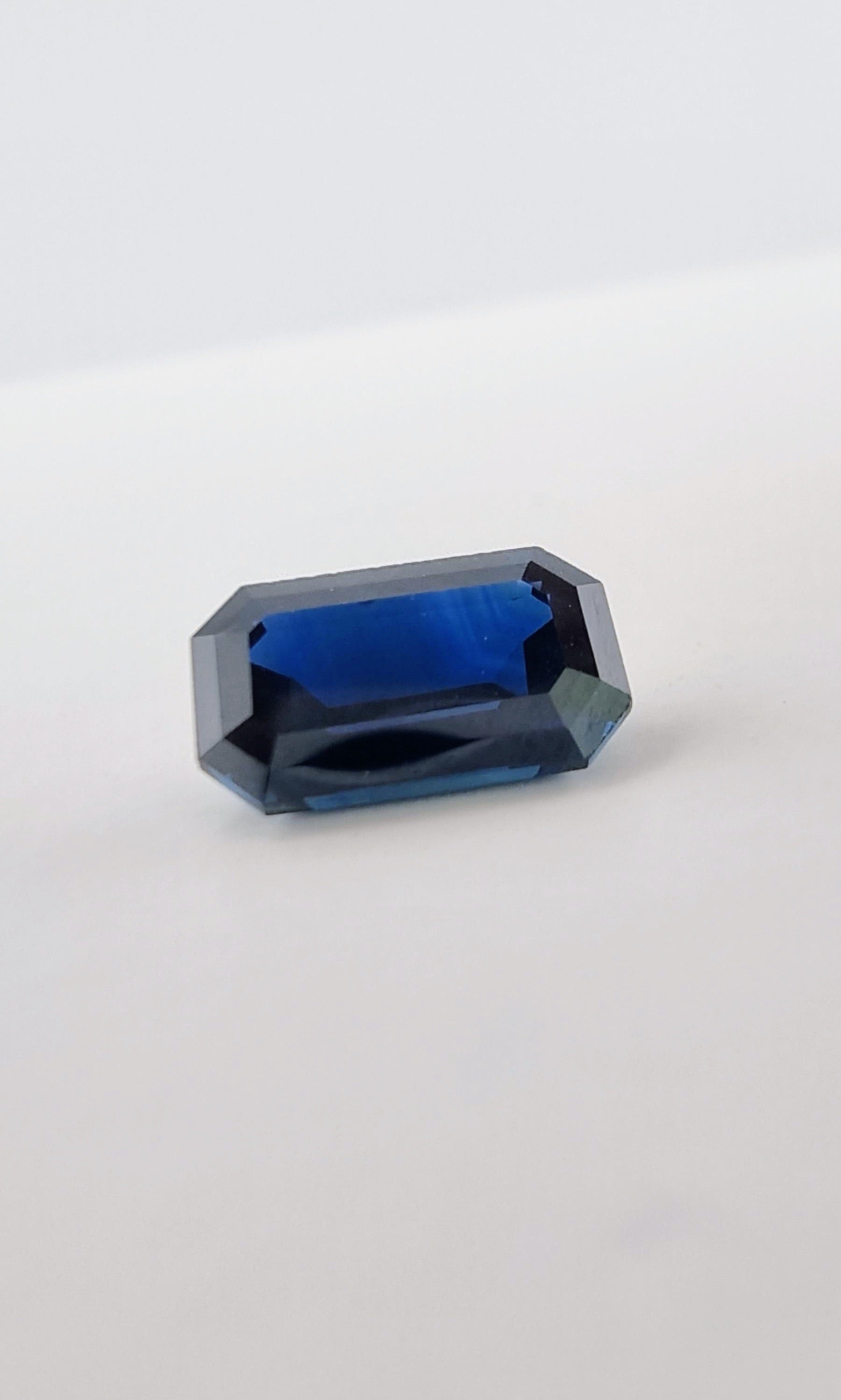Side angle of 2.1ct rectangular cut dark blue natural sapphire gemstone highlighting its transparency and elegant faceting.