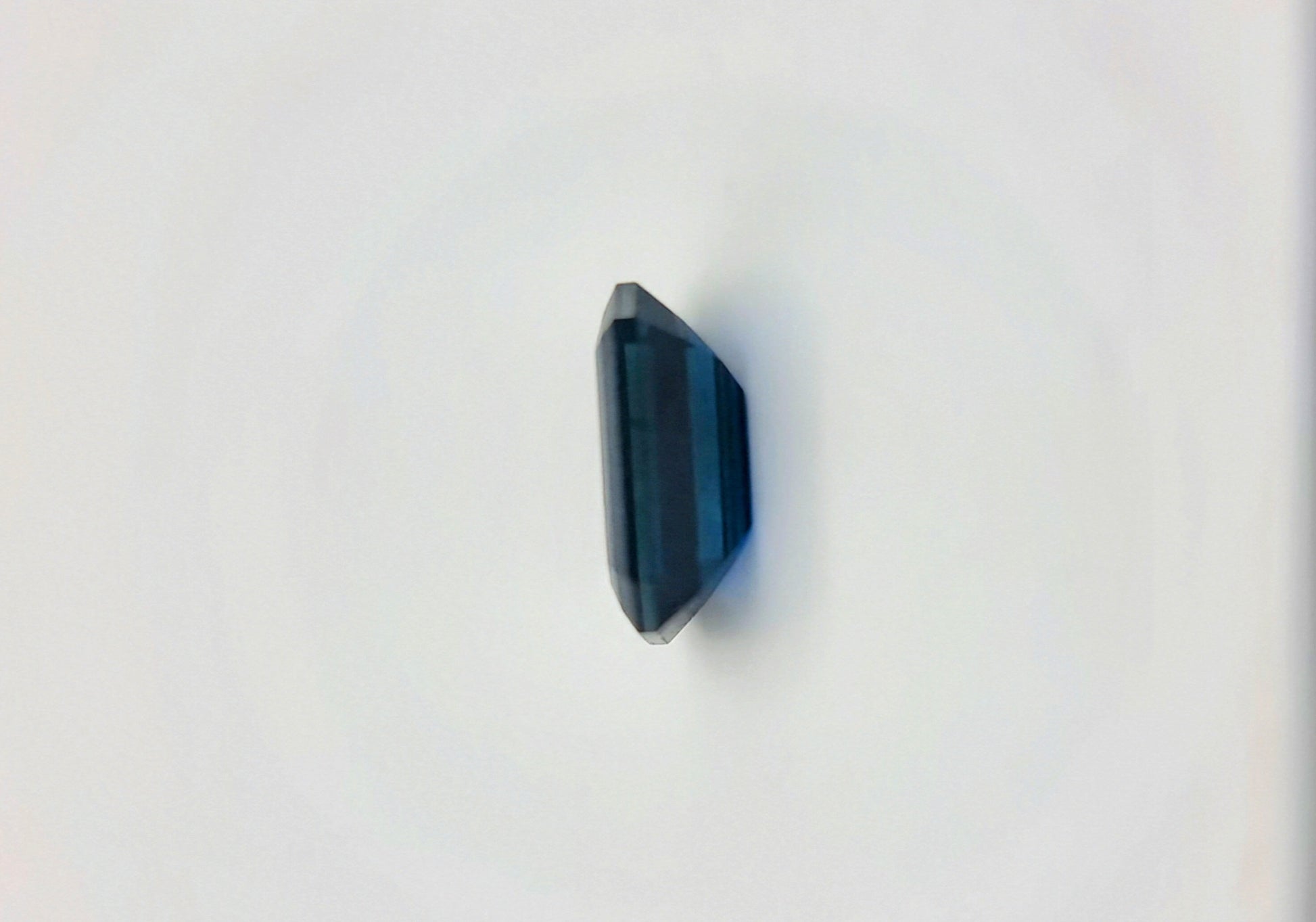 Vertical side view of 2.1ct rectangular cut dark blue natural sapphire gemstone emphasizing its thickness and geometric precision.