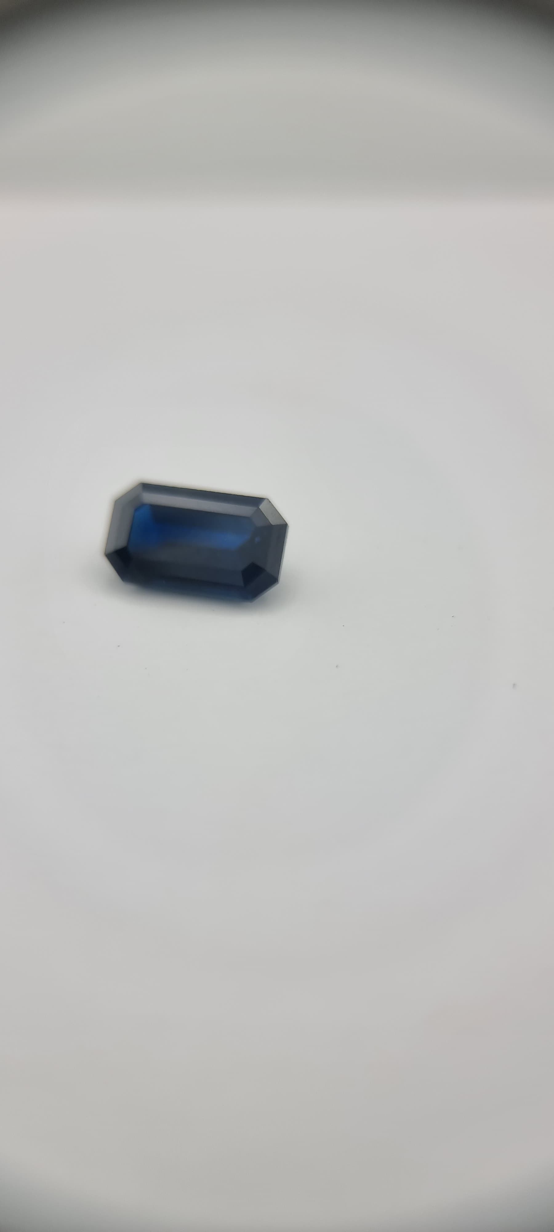 Angled view of 2.1ct rectangular cut dark blue natural sapphire gemstone on white background, ideal for gemstone collectors and artisans.
