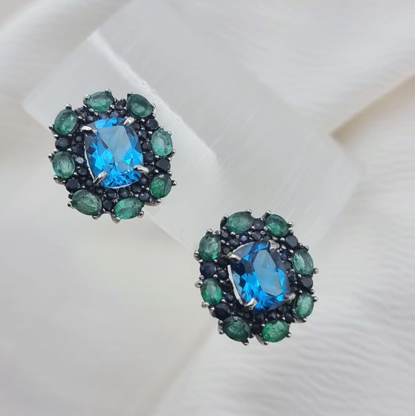 Natural Topaz Emerald & Sapphire Platinum Earrings on white display, showcasing the radiant blue topaz and contrasting green emeralds.