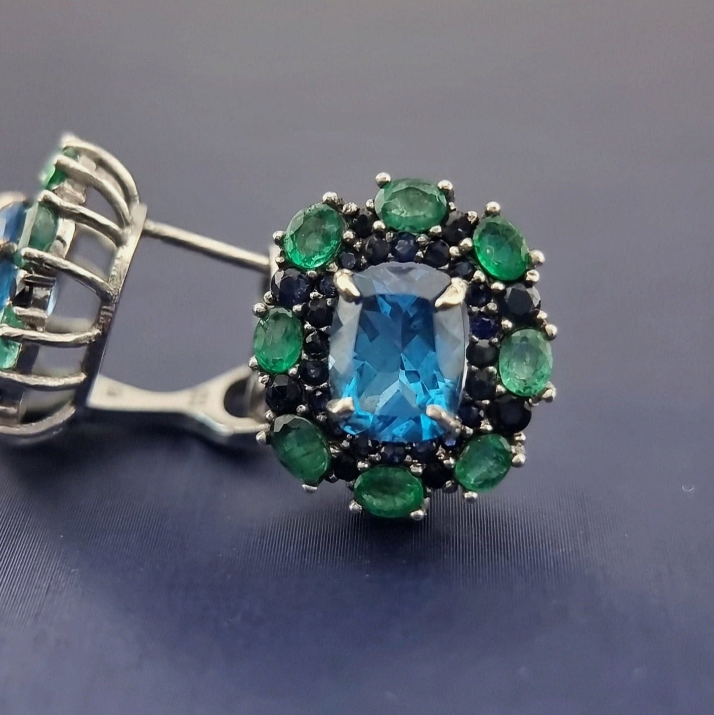 Natural Topaz Emerald & Sapphire Platinum Earrings in close-up, highlighting the vibrant blue topaz and surrounding green emeralds.