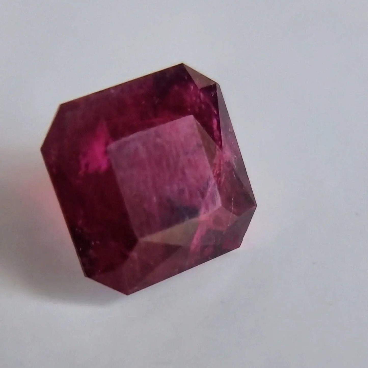 Angled view of 13.16ct red Rubellite Tourmaline gemstone in square cut, highlighting its brilliance and faceted clarity.