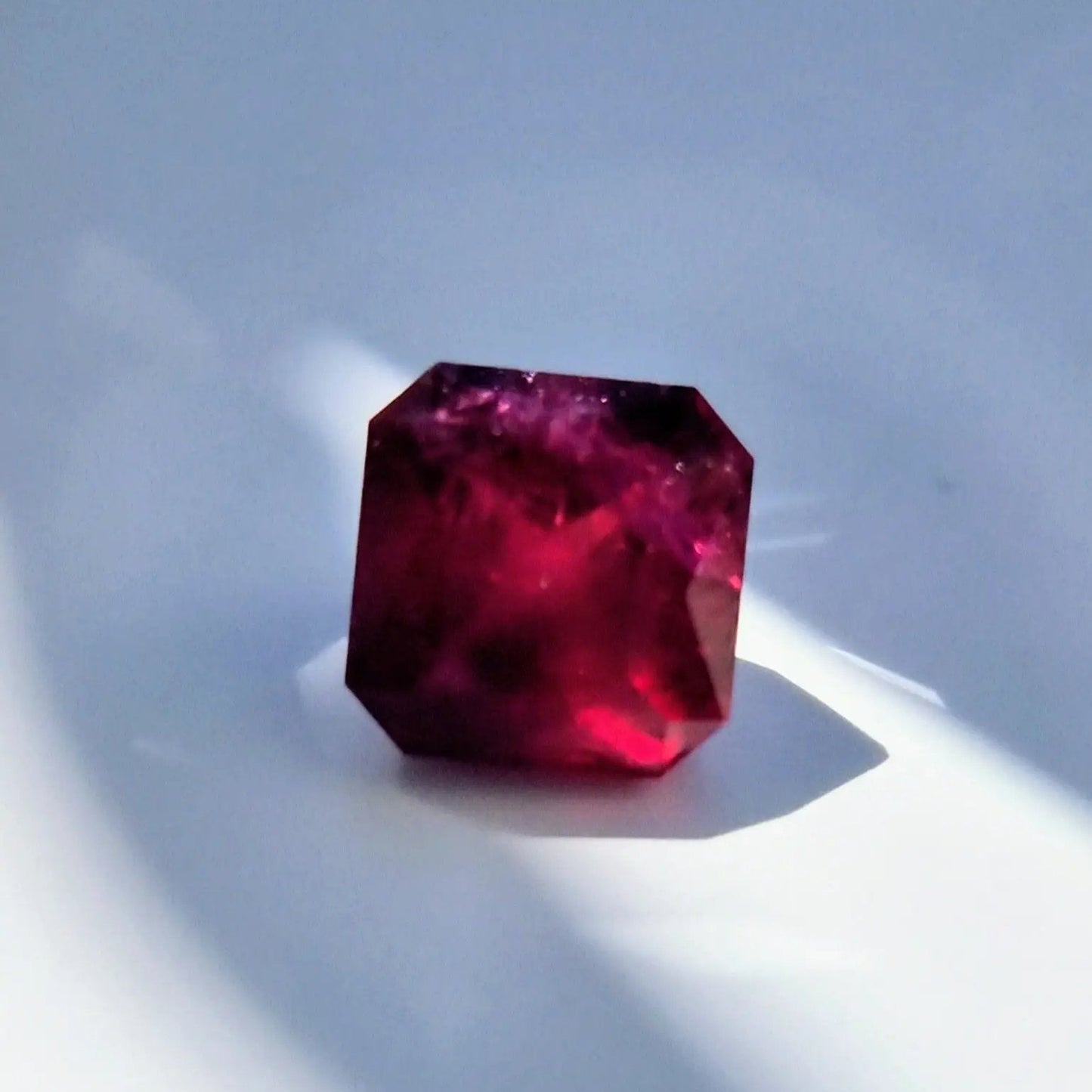 13.16ct square cut Rubellite Tourmaline gemstone under natural light, revealing its rich red color and internal clarity.