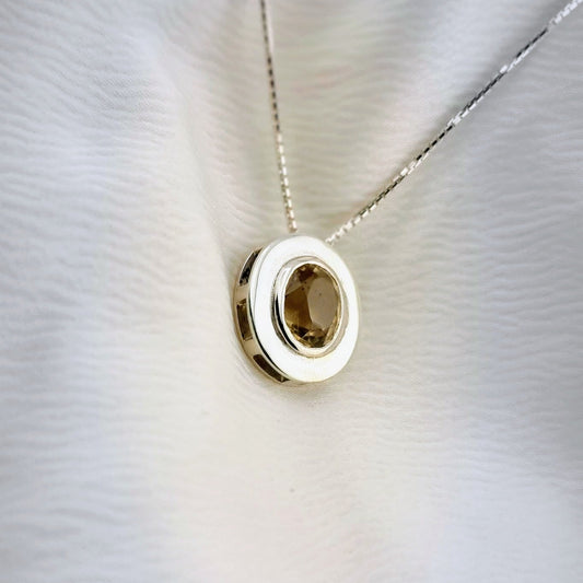 Sterling silver citrine pendant necklace with a round unheated gemstone, displayed on a soft white fabric to highlight its warm yellow hue.