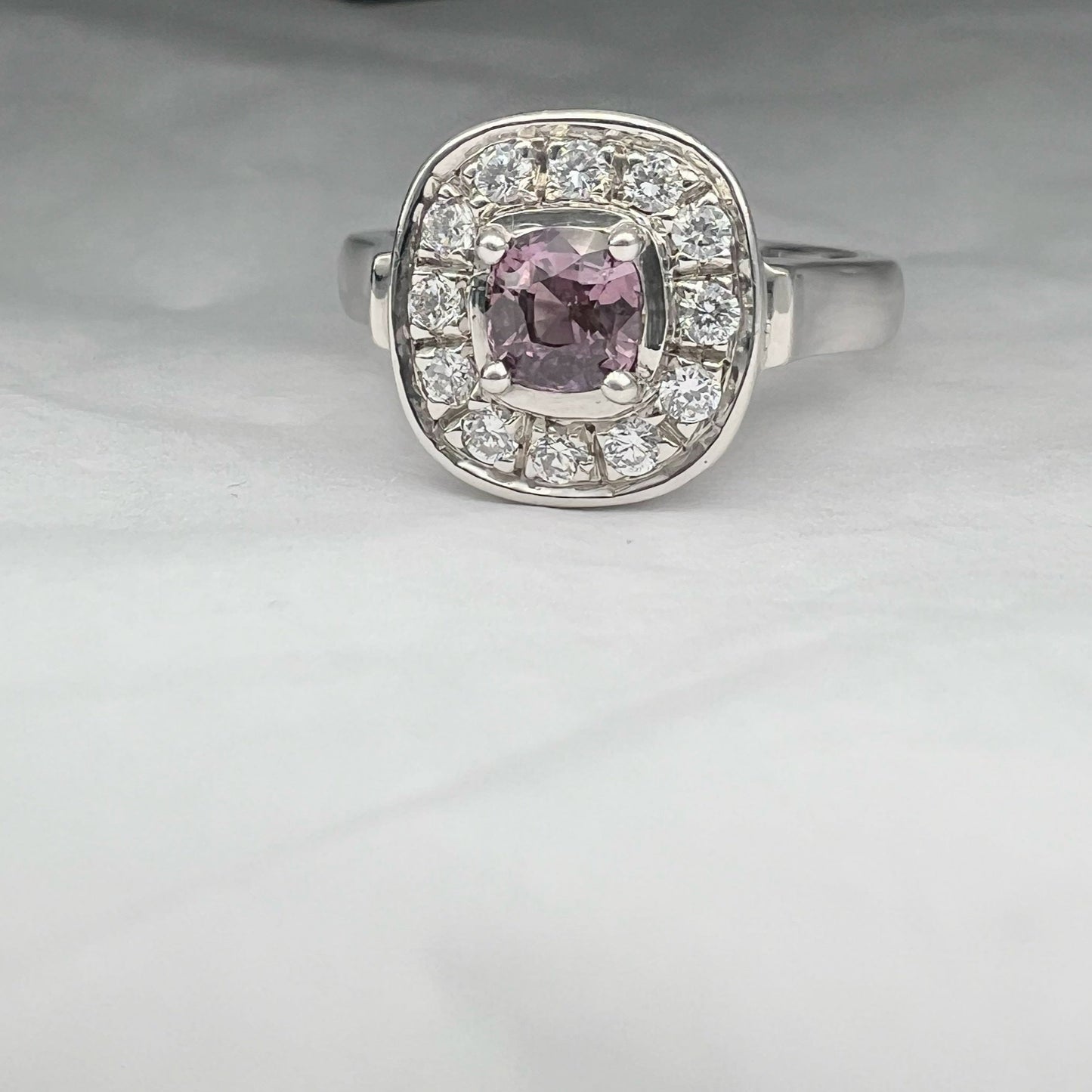 Elegant pink sapphire ring with cushion-cut center stone and diamond halo in platinum silver. A unique jewelry piece perfect for stylish accessorizing.