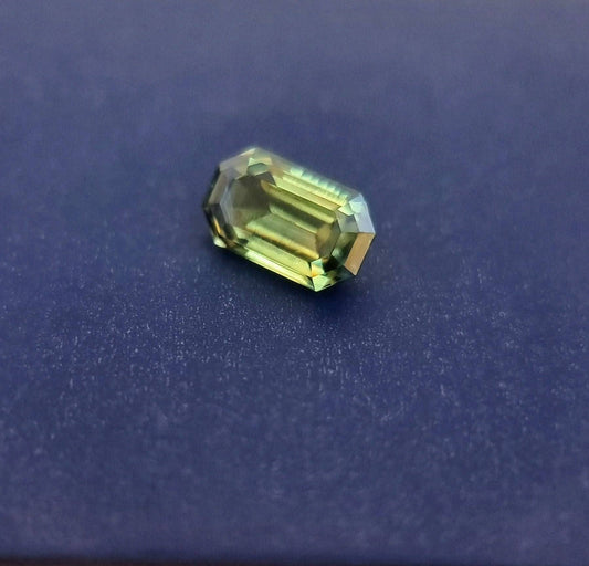 Natural teal blue sapphire gemstone with an emerald cut resting on a dark surface, highlighting its clarity and exquisite faceting.