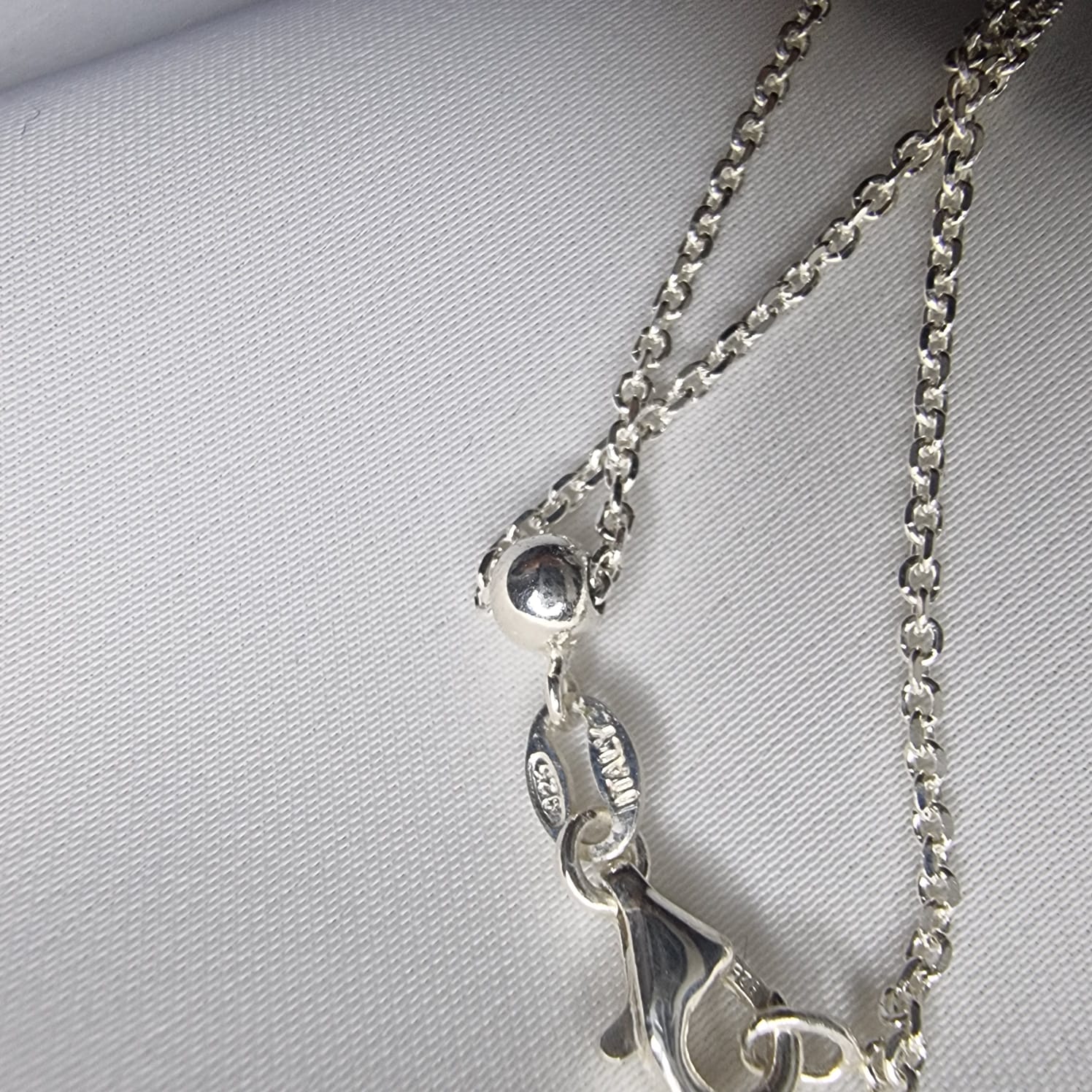 a close up of a silver necklace on a white background