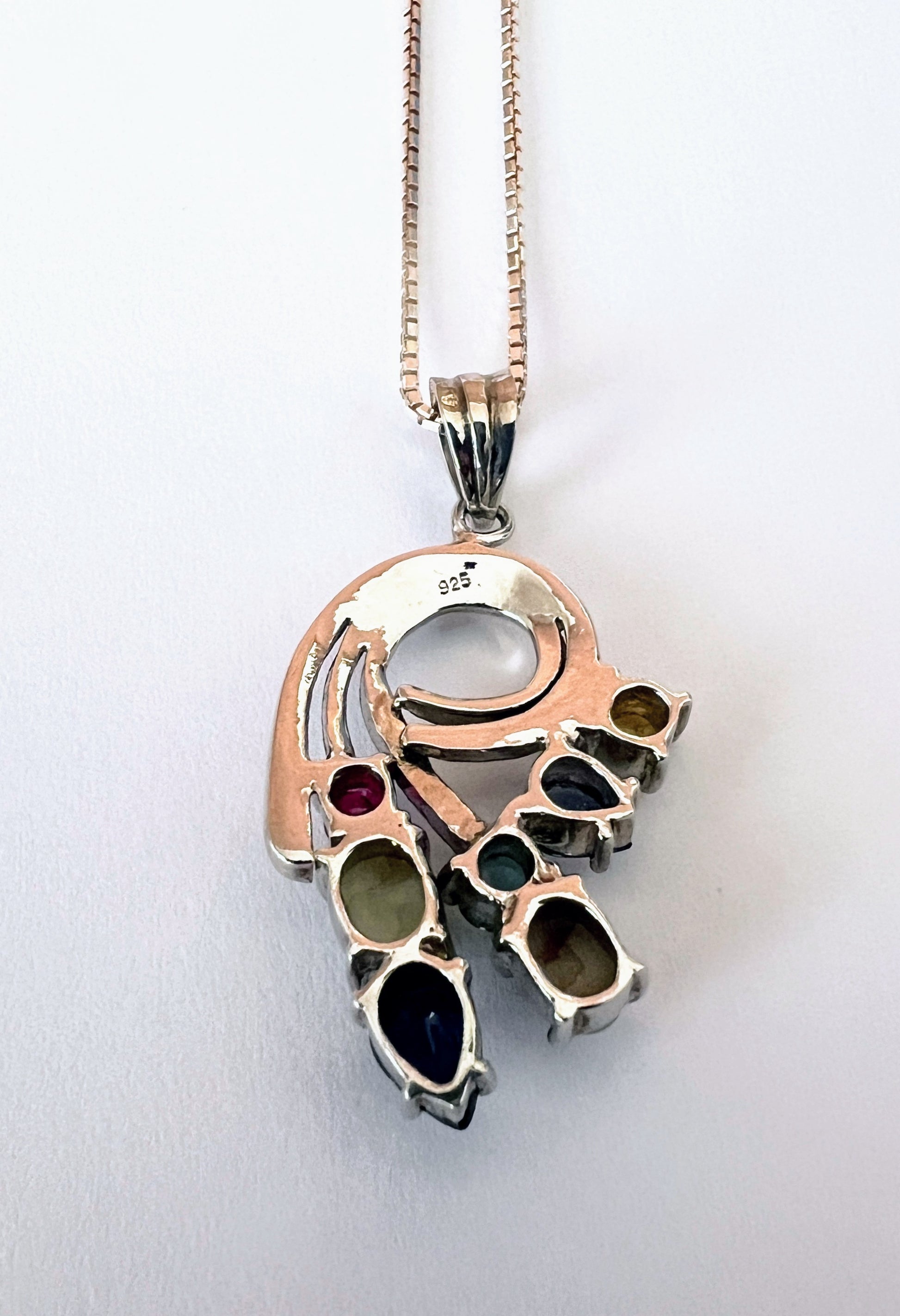 Sterling silver Multigem Swirling Infinity Pendant Necklace showing gemstone settings and 925 stamp. Includes ruby, emerald, and sapphire in floral swirl design.
