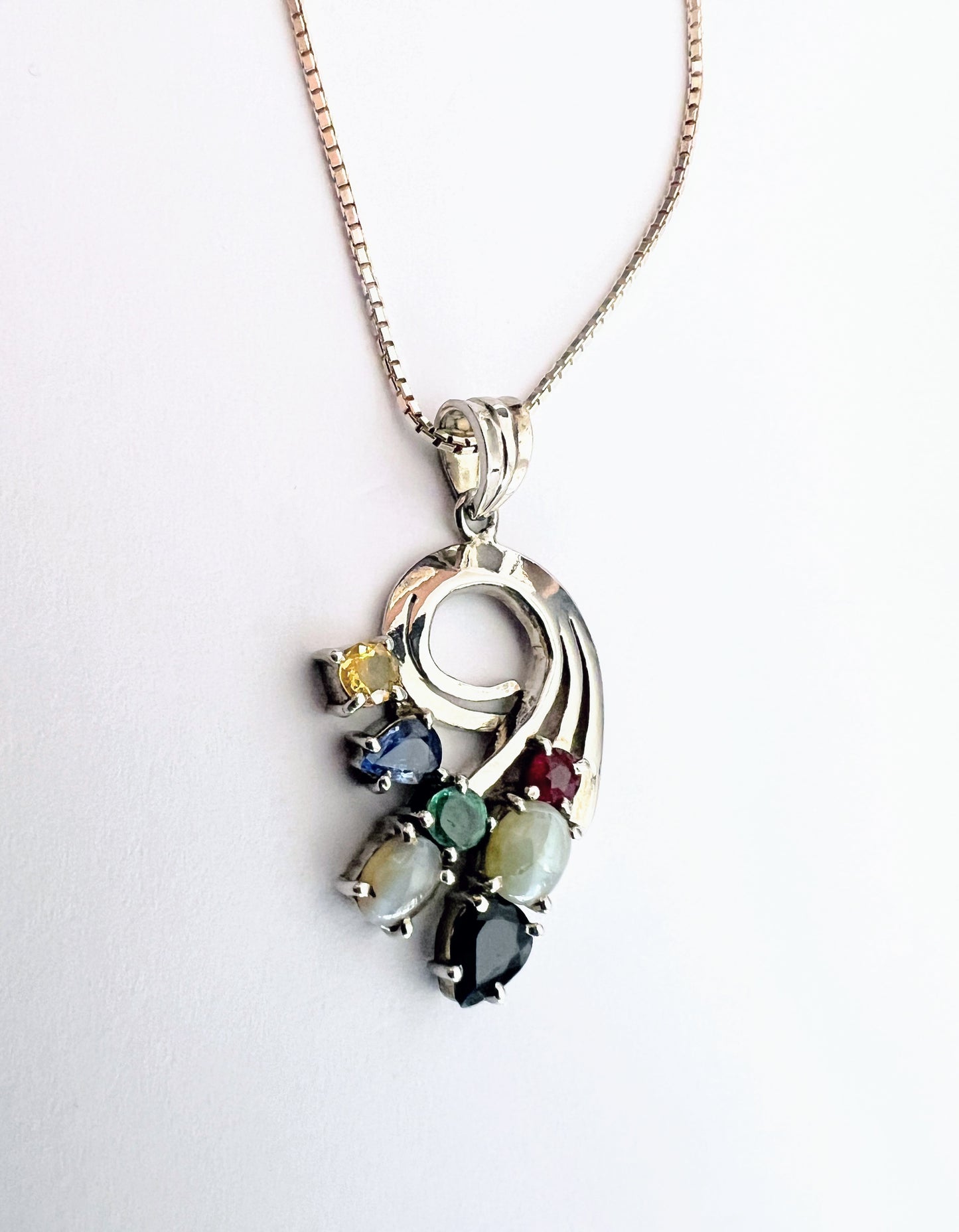 Front view of Multigem Swirling Infinity Pendant Necklace with vibrant gemstones including ruby, emerald, and sapphires. Floral swirl design on silver chain.