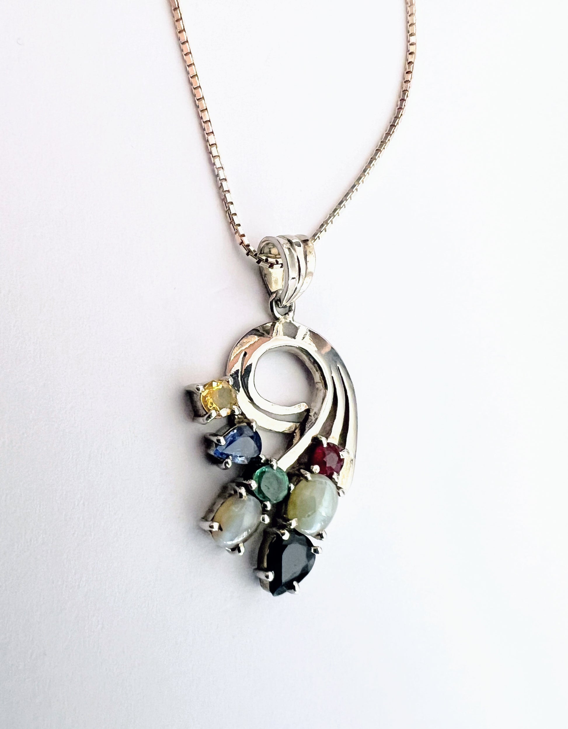 Front view of Multigem Swirling Infinity Pendant Necklace with vibrant gemstones including ruby, emerald, and sapphires. Floral swirl design on silver chain.