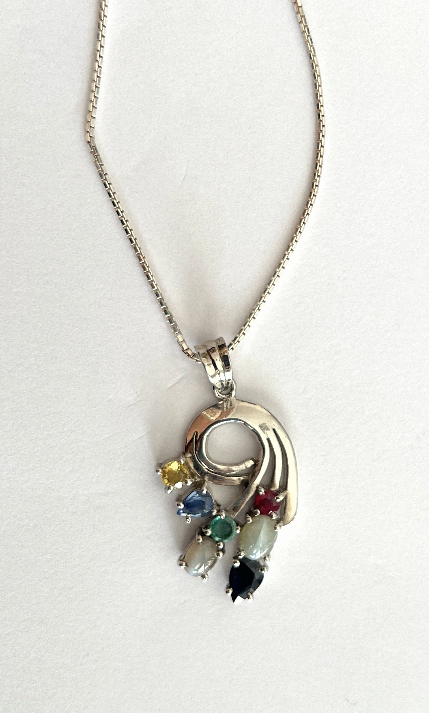 Full view of Multigem Swirling Infinity Pendant Necklace with ruby, sapphires, emerald, and cat's-eyes. Elegant floral motif in sterling silver for fine jewelry lovers.