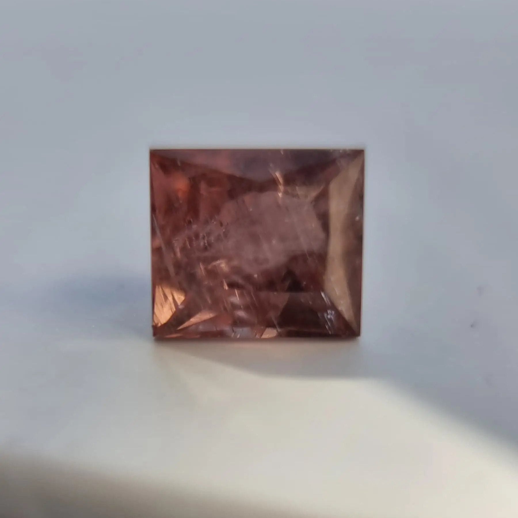 Close-up of square cut red tourmaline gemstone with rich rust-red color and sharp faceting, ideal for jewelry making.