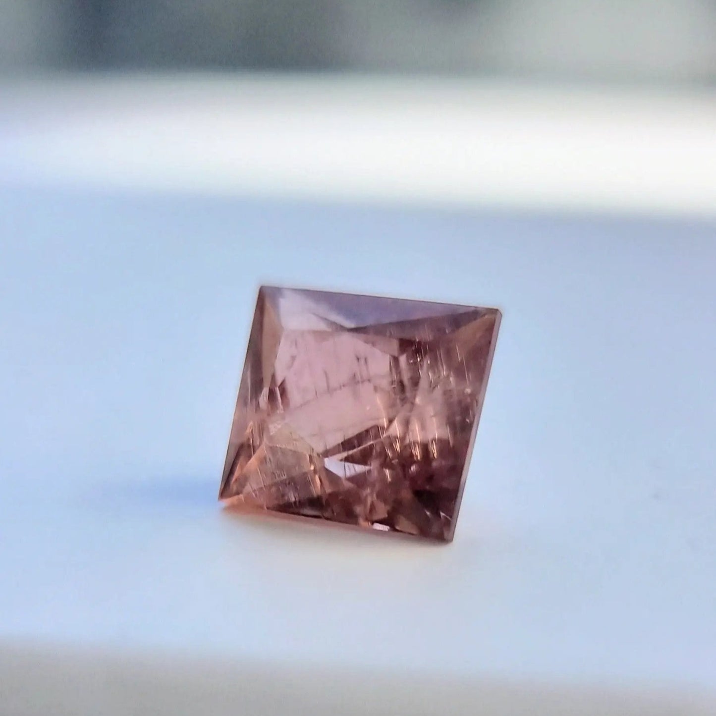 Angled display of 5.13 carat square cut red tourmaline gemstone with warm rust-red color and faceted brilliance.