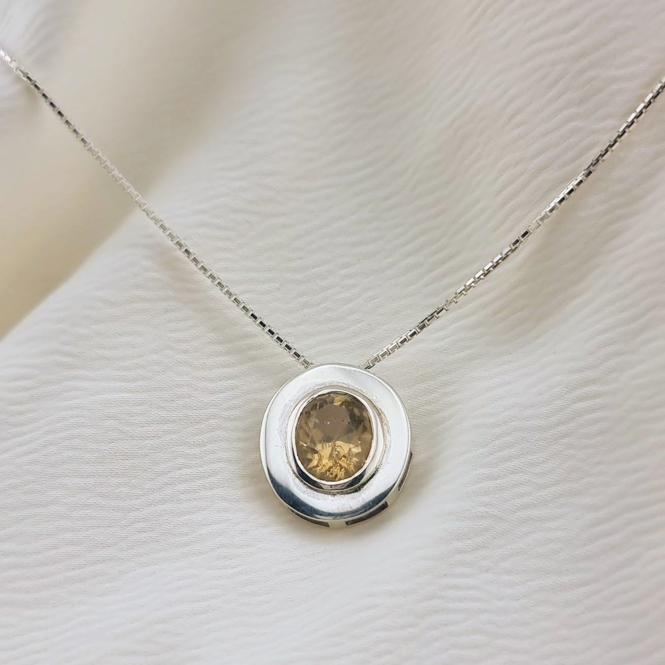 Natural unheated citrine pendant necklace in sterling silver resting on textured fabric, showcasing its warm tone and elegant circular design.
