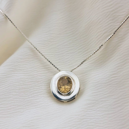 Natural unheated citrine pendant necklace in sterling silver resting on textured fabric, showcasing its warm tone and elegant circular design.