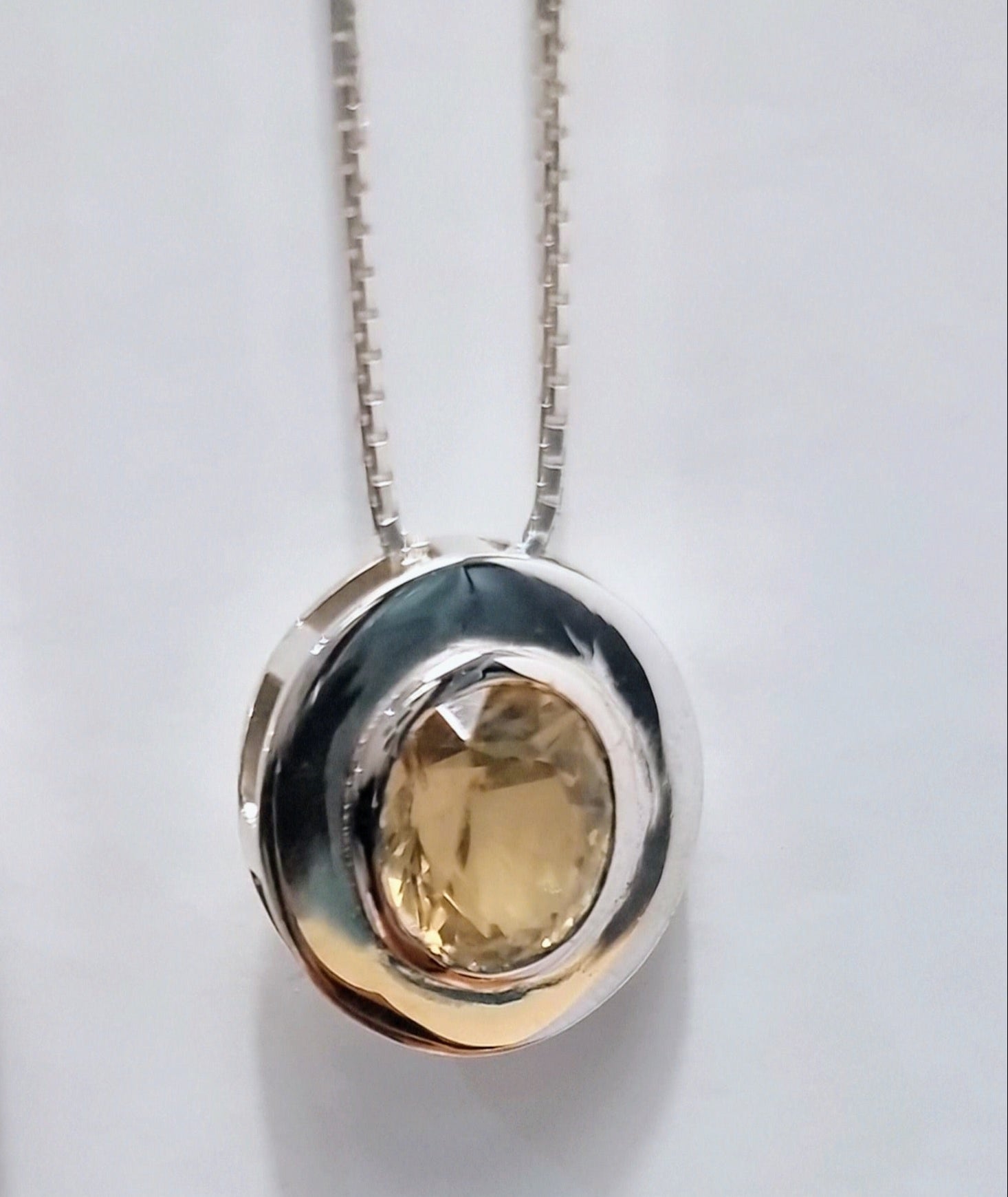 Detailed view of citrine pendant necklace in sterling silver featuring a faceted natural gemstone in a modern circular bezel setting.