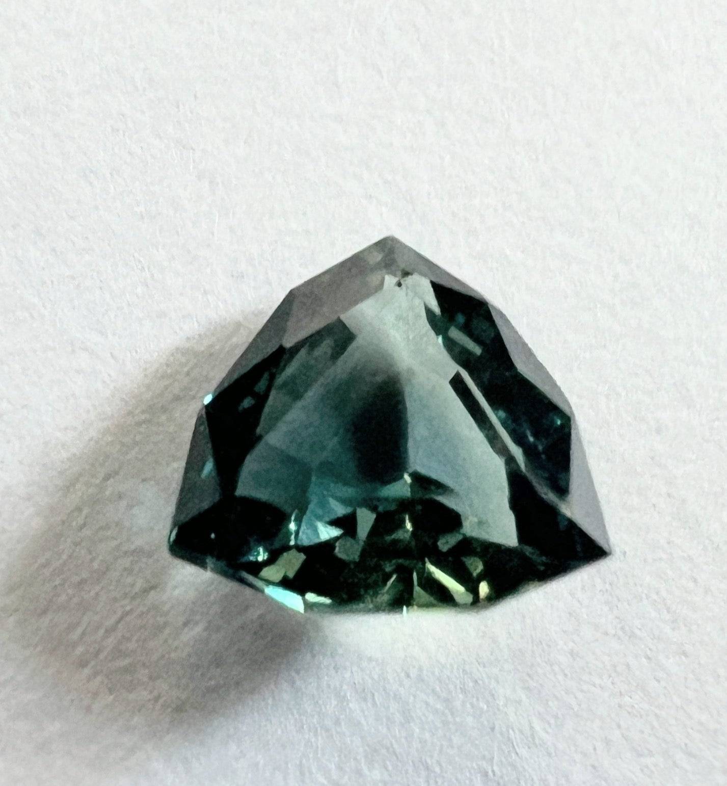 Close-up of a trillion cut teal blue sapphire gemstone with intricate facets, reflecting light beautifully for jewelry making.