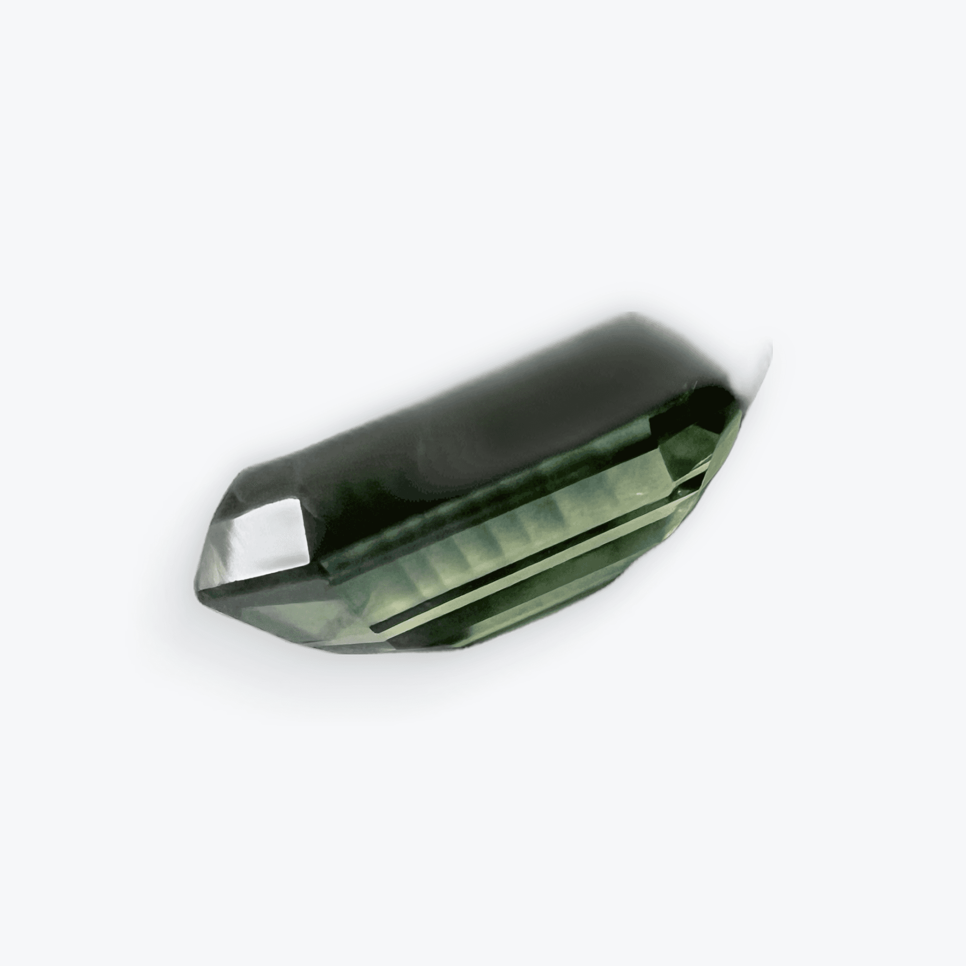 Side view of an emerald cut teal blue sapphire gemstone, highlighting its depth, clarity, and intricate faceting against a white background.