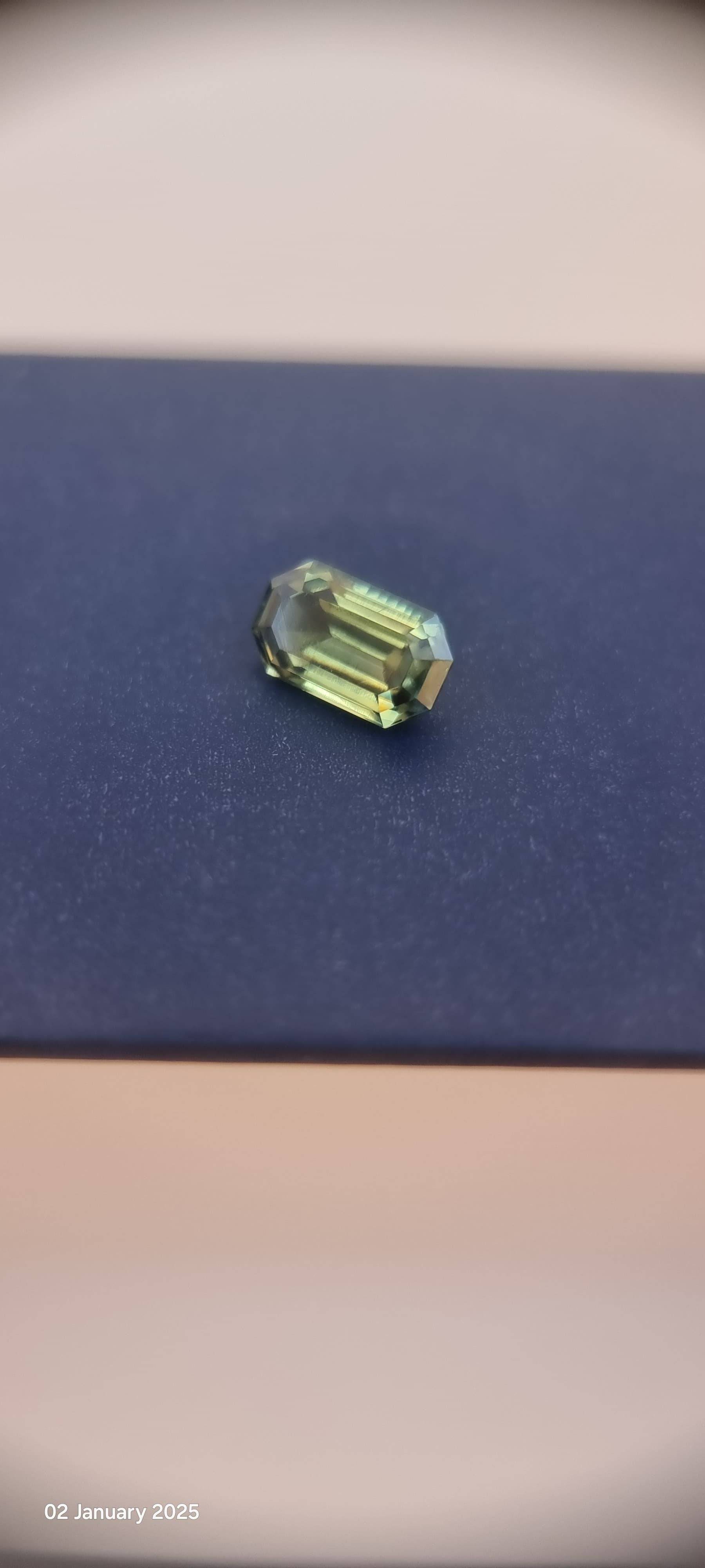 Loupe clean emerald cut teal blue sapphire gemstone placed on a dark surface, capturing its brilliance and natural color variations.