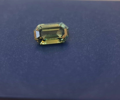 Loose teal blue sapphire gemstone with an emerald cut placed on a dark surface, highlighting its natural brilliance and faceted design.