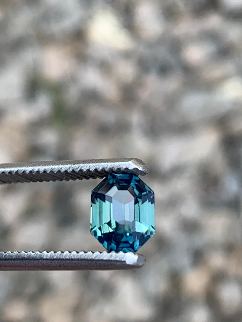 A radiant cut 2.5ct blue teal sapphire gemstone held by tweezers, emphasizing its untreated natural beauty and elegant sparkle.