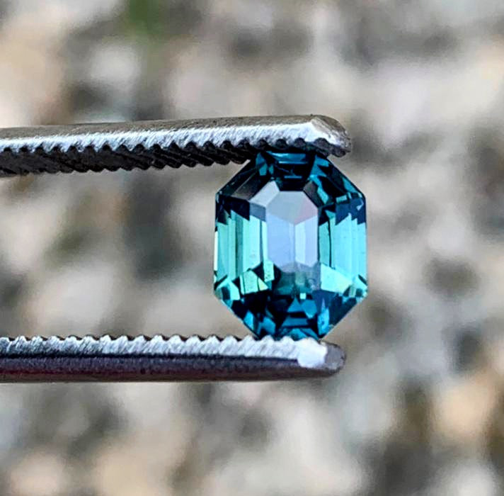 Brilliant 2.5ct radiant cut blue teal sapphire gemstone held by tweezers, reflecting light with mesmerizing depth and clarity.