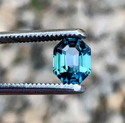 Brilliant 2.5ct radiant cut blue teal sapphire gemstone held by tweezers, reflecting light with mesmerizing depth and clarity.
