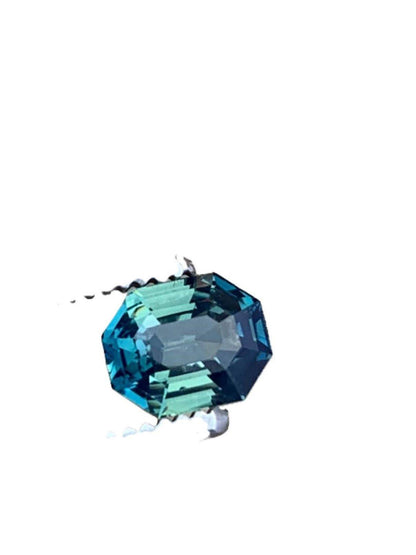 Loose 2.5ct radiant cut blue teal sapphire gemstone displayed against a white background, highlighting its exquisite cut and color.