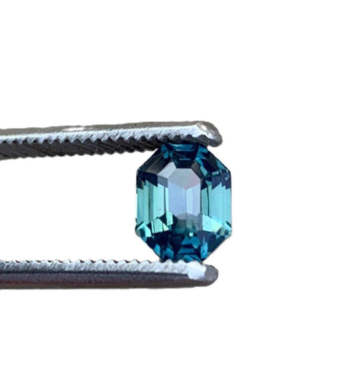 2.5ct radiant cut untreated blue teal sapphire gemstone held by tweezers, showcasing its vibrant color and brilliant facets.