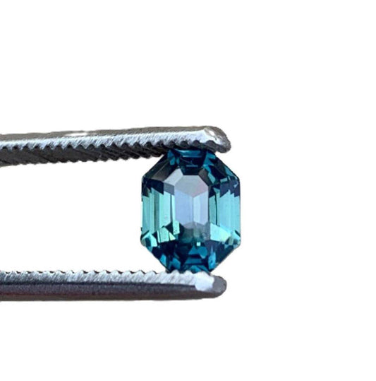 2.5ct radiant cut untreated blue teal sapphire gemstone held by tweezers, showcasing its vibrant color and brilliant facets.